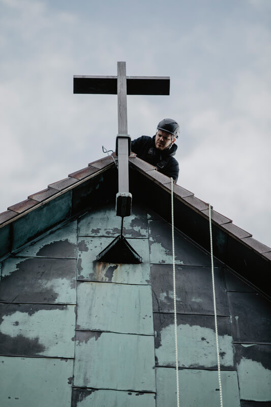 Industriekletterer kontrolliert Kreuzbefestigung auf einem Kirchendach