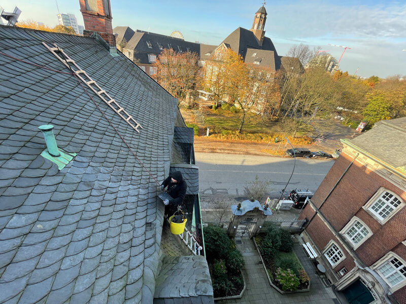 Industriekletterer schlägt auf einem Dach eine Schieferplatte zu